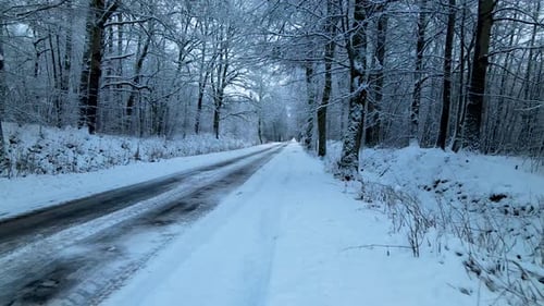 Low angle drone flying along the snow-covered and ice-covered countryside forest road, huge snowdrif