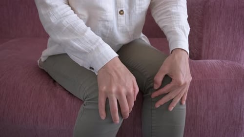 Mãos femininas segurando a dor no joelho em ambientes fechados.