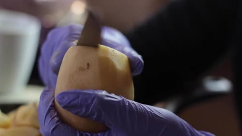 Close up of hands with purple gloves slicing potato into thin disks