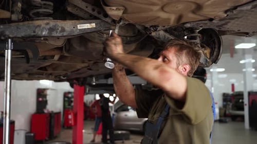 Auto Mechanic Repairs Car Suspension in Garage Skilled Technician Uses Wrench Under Vehicle Focuses