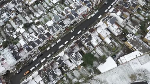 Flying with drone over rooftops of London neighborhood during snowfall, UK. Aerial view