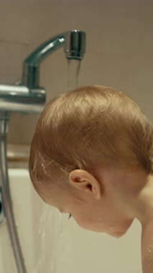 Vertikale Darstellung eines entzückenden kleinen Jungen, der den Kopf unter Wasser legt, das aus dem Wasserhahn läuft