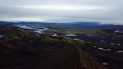 Vista aérea de paisaje con un dron de una persona con una chaqueta roja, de pie en la cima de una montaña, en