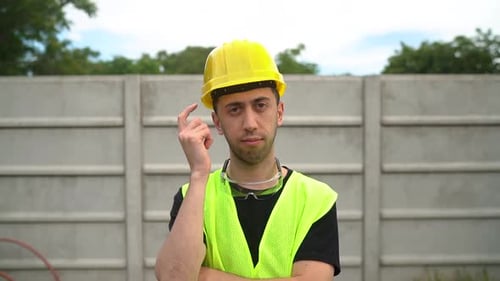 Construction Worker In Yellow Hard Hat And Reflective Vest Pointing Finger To Head. medium shot