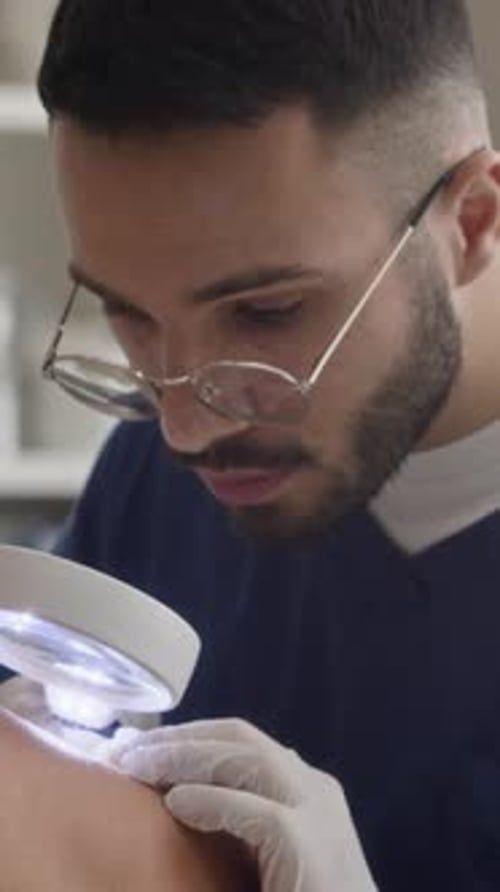 Vertical of Middle Eastern Dermatologist Examining Skin with Magnifying Glass