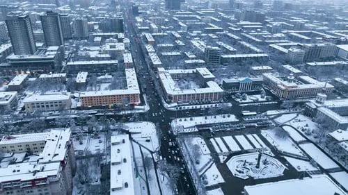 Aerial view of a snowy city block, intersection and public square in Bishkek