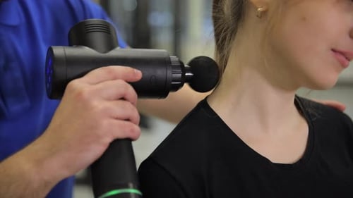 A Therapist Uses a Percussion Massage Gun on a Womans Neck for Effective Muscle Relief and Recovery