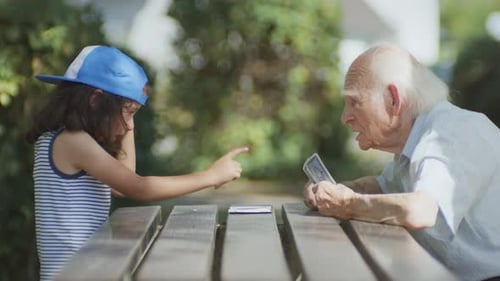 Grandfather and granddaughter playing cards in the city park, it looks like the grandfather is serio
