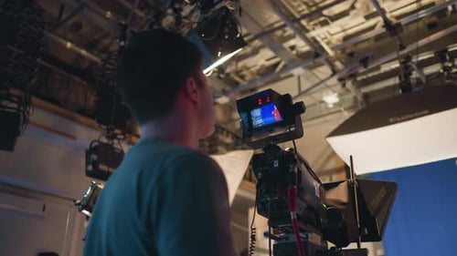 Cameraman Operating Video Camera During Studio Shoot with Blue Screen Background