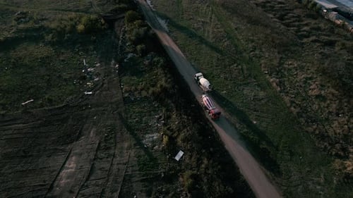 Aerial static shot of two cement mixer trucks meeting on a dusty road 4K