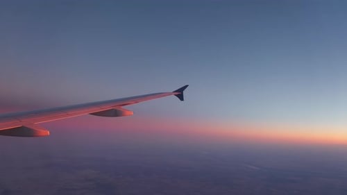 Aircraft Wing of Flying Above Clouds Airplane As Seen By Passenger Through Porthole on Sunset