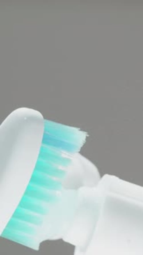 Vertical video. Squeezing toothpaste onto a toothbrush and showing it in close-up. Blue bristles.
