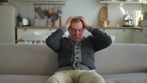 Dolor de cabeza Hombre mayor infeliz de mediana edad que sufre de dolor de cabeza frotándose las sienes en casa