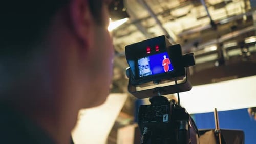 Camera Operator Monitoring Presenter on Blue Screen Stage During Studio Production