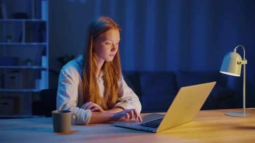 Young Woman Reading on Laptop at Table in Evening Folding Hands in Quiet Prayer