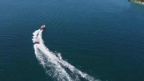Aerial tracks boat towing raft of happy tourists on bright sunny day