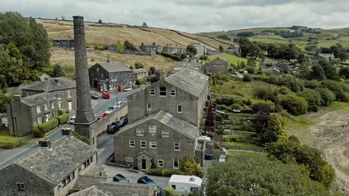 Rooftop Aerial footage of a industrial rural village with old mill and chimney stack surrounded by f
