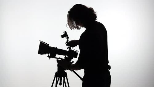 Silhouette of Cinematographer Adjusting Film Camera Settings