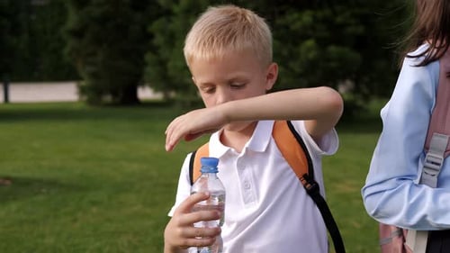 Schoolboy Opens a Water Bottle in the School Yard and Douses Himself with Water