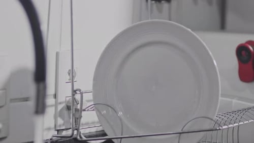 Close up, person's arm hanging ceramic cup on drying rack after washing in kitchen sink