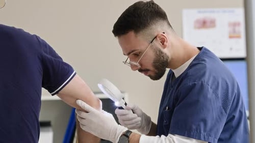 Young Middle Eastern Male Doctor Examining Skin on Elbows with Magnifying Glass