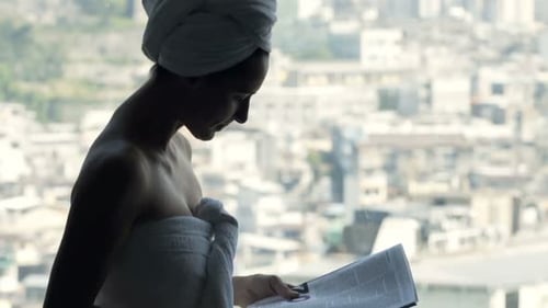 Woman In Towel Reading Magazine And Drinking Coffee Standing By Window At Home