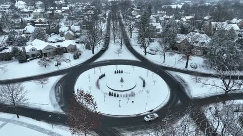 Aerial view of large traffic circle in winter. Snow on ground and cars driving in American housing d