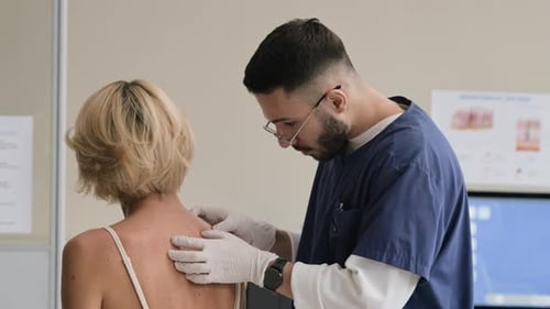 Young Male Doctor Examining Moles of Female Patient in Clinic
