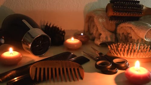 Close up shot of hairdresser tools, brushes, scissors, combs, hair dryer, towels, next to some candl