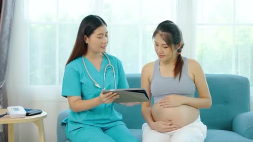 Beautiful female nutritionist uses a tablet to suggesting something to young pregnant Asian woman