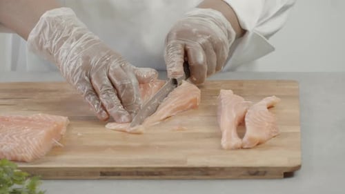 close up of chef's hand cutting chicken. Man cutting fresh meat with knife on wooden cutting board.