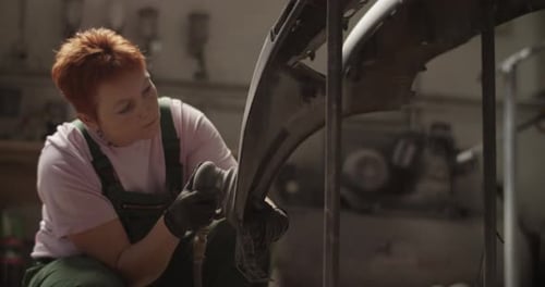 Focused Female Tradie Sanding Car Bumper in Daytime