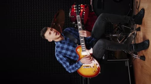 Stylish male musician singing song and playing on electric guitar. Vertical video