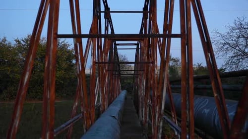 Passage through the construction of an old rusty iron bridge leading over a narrow river during an a