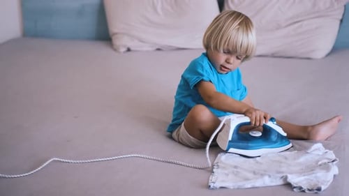 a Small Child Irons His Clothes on the Bed