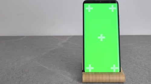 a Phone with a Green Screen is on a Wooden Stand