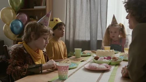 Crianças e mulheres reunidas ao redor da mesa com bolo de aniversário e doces