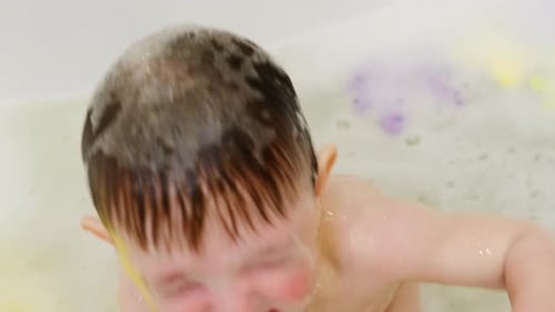 Der Vater gießt Wasser aus einer Kelle in einer weißen Wanne über das Baby. Ein glückliches Kind wird darin gewaschen