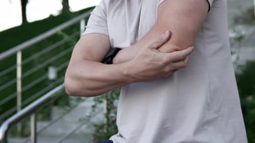 A man feels acute pain in his elbow joint while walking in the evening. Sports and injury concept.