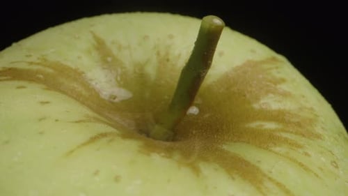 A drop of water falls into the recess of a green apple. Slow motion, macro photography.