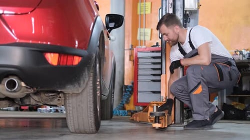 A Skilled Man in a Uniform Fixes a Car He Examines It From All Sides