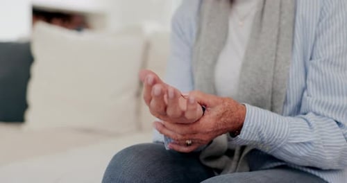 Hands, arthritis or carpal tunnel with a senior person on a sofa in the living room of a retirement