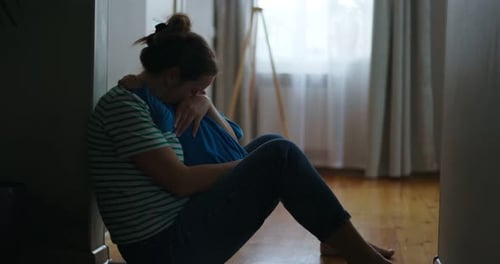 Sad Woman Sitting on Floor of Her Apartment Hugging Her Little Child