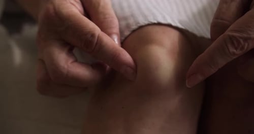 Vista desde arriba de las manos de un jubilado de cerca frotándose un quiste poplíteo o sinovial, una hinchazón llena de líquido