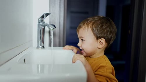 Baby boy rejoices opening the water tap.