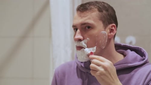 Man Shaving in Bathroom With Foam on His Face and Relaxed Expression While Preparing for the Day