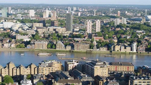 Aerial drone shot following a barge navigating through the Thames on a warm summer day. A range of a