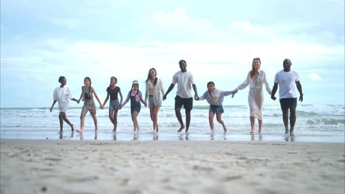 Group of diverse friends having fun at the beach, walking and jump in the waves on a sunny day
