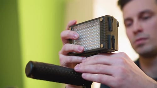 Lighting Operator Adjusting LED Light Panel While Preparing Camera Setup for Filming