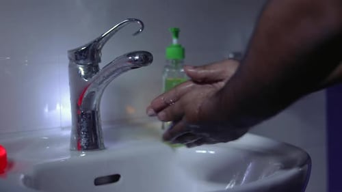 A man washing hands with hand wash in a wash basin.